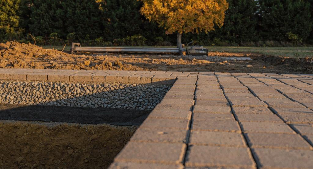 Paver patio under construction showing the compacted aggregate base and geotextile fabric layers that hardscaping in Kansas City requires